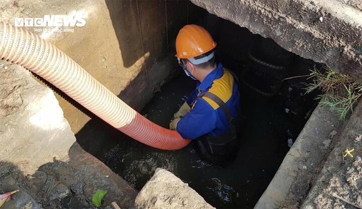 Công nhân thoát nước lội sâu xuống hố ga, vận hành ống bơm hút bùn và rác thải.