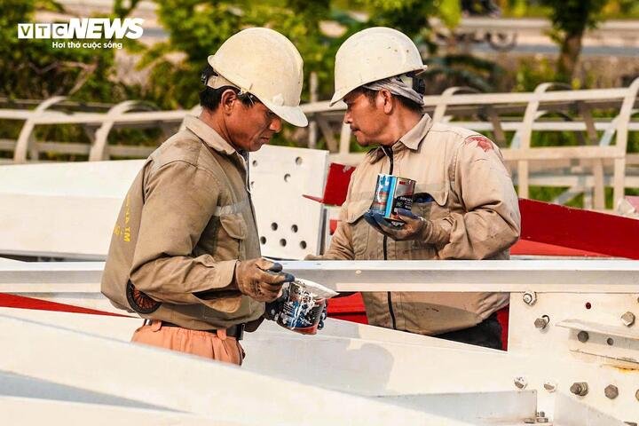 Ở mặt đất, các tổ thợ cũng tất bật với khối lượng công việc không kém phần vất vả. Người sơn hoàn thiện các cấu kiện thép, người buộc, cố định từng bộ phận để chuẩn bị cho việc cẩu kéo lên cao.