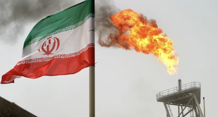 Ngọn lửa khí đốt trên giàn khoan dầu nằm cạnh lá cờ Iran ở vùng Vịnh. (Ảnh: Reuters)