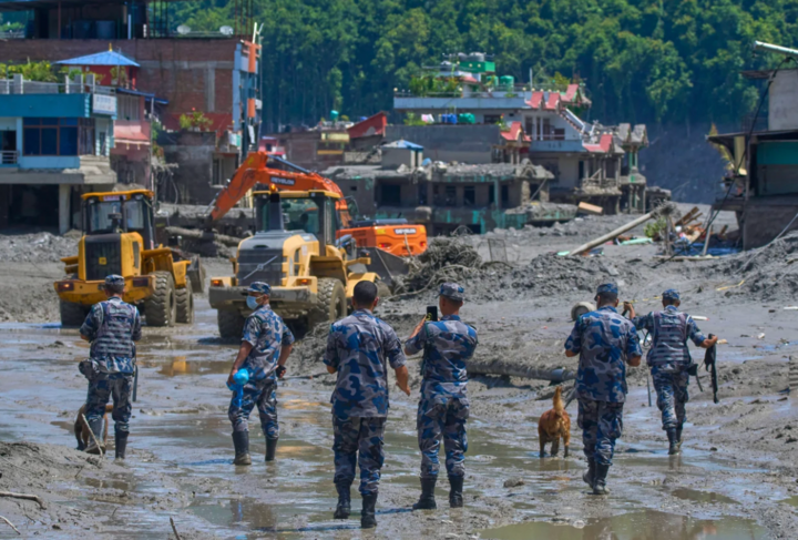 Cảnh sát Nepal quan sát khi máy xúc dọn dẹp đống đổ nát sau trận lũ quét. (Ảnh: AP)