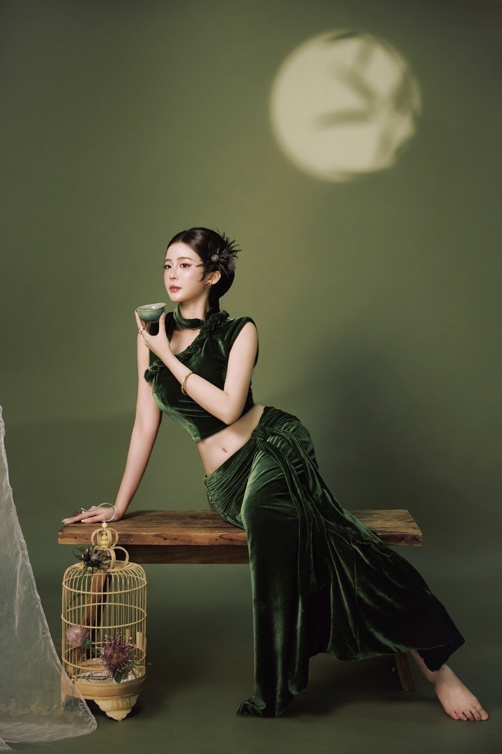 Ở loạt ảnh đầu, cô diện trang phục nhung xanh đậm, tạo dáng bên lồng chim và tấm voan mỏng. Ánh sáng dịu cùng gam màu trầm mang đến cho khung hình vẻ huyền ảo, gợi liên tưởng đến một đêm Trung thu dưới ánh trăng rằm.