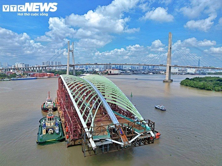 Tổ hợp kết cấu được lai dắt từ Vũng Tàu về TP.HCM có tổng trọng lượng khoảng 3.400 tấn, gồm nhịp chính vòm thép dài 187 m, nặng 1.400 tấn và hệ khung đỡ chuyên dụng nặng khoảng 2.000 tấn. Hiện sà lan chở kết cấu này neo dọc bờ sông phía Thủ Thiêm, chờ đưa vào vị trí lắp đặt.